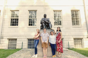 4 students standing in front of John Harvard statue in Harvard Yard