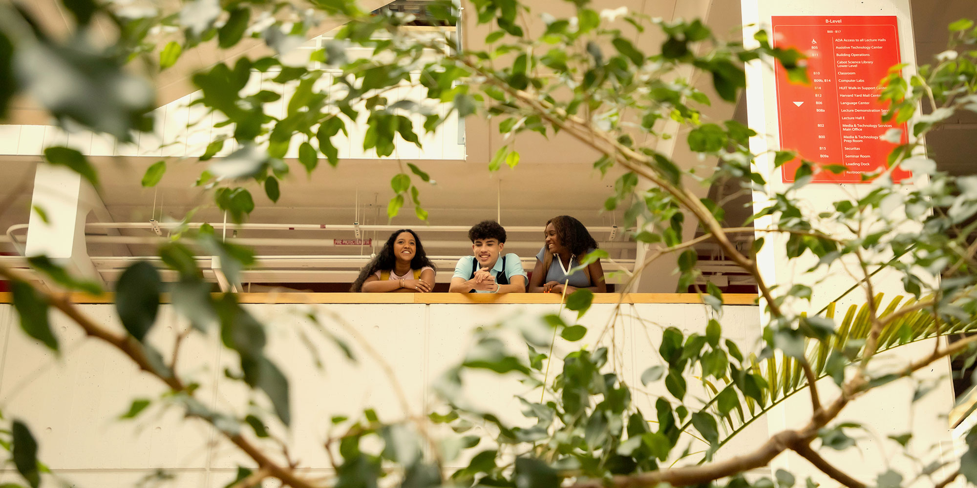 Three students look out over an internal balcony on the Harvard campus.